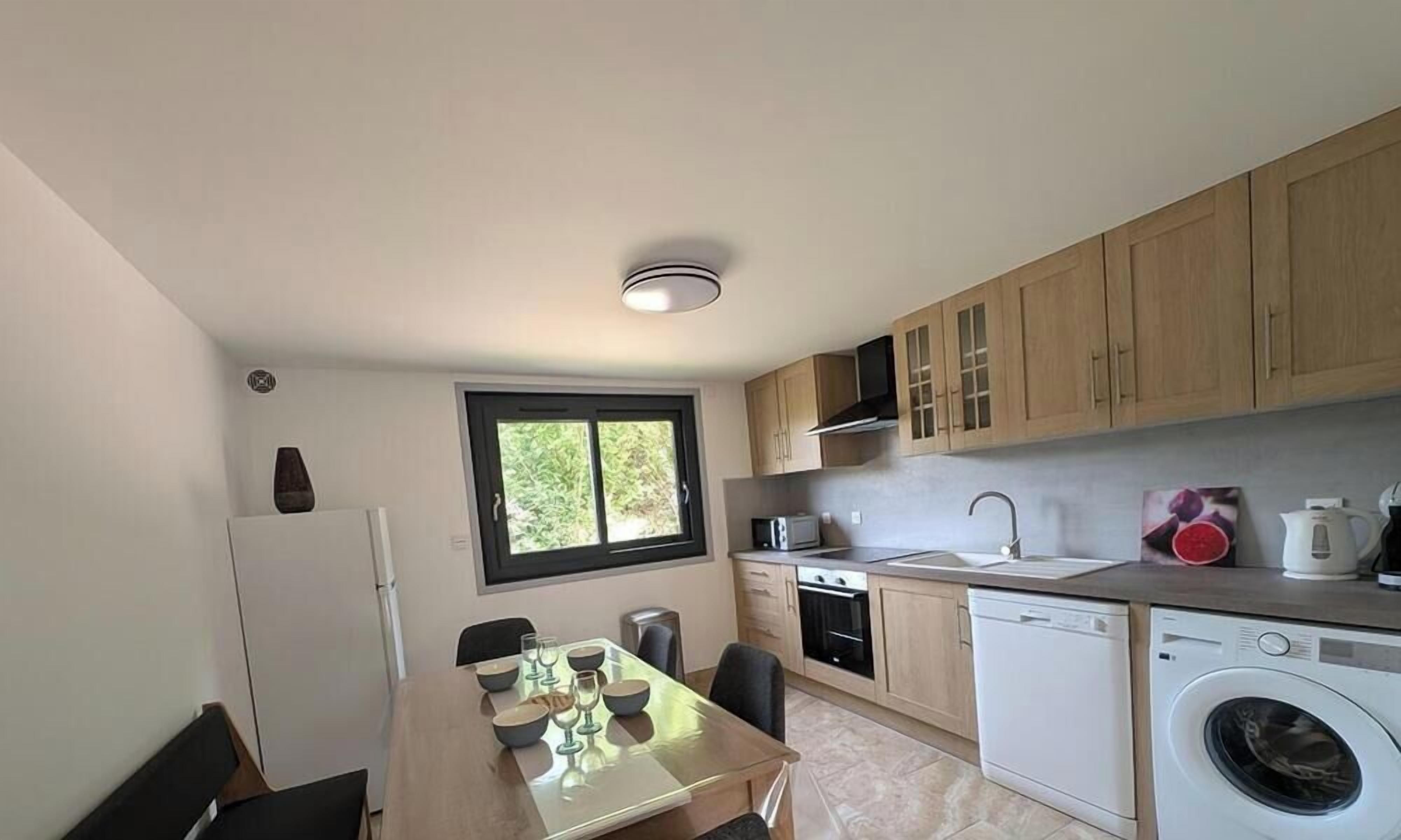 A compact kitchen with a dining area, a built-in oven, a washing machine, and a window providing natural light.