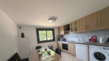 A compact kitchen with a dining area, a built-in oven, a washing machine, and a window providing natural light.