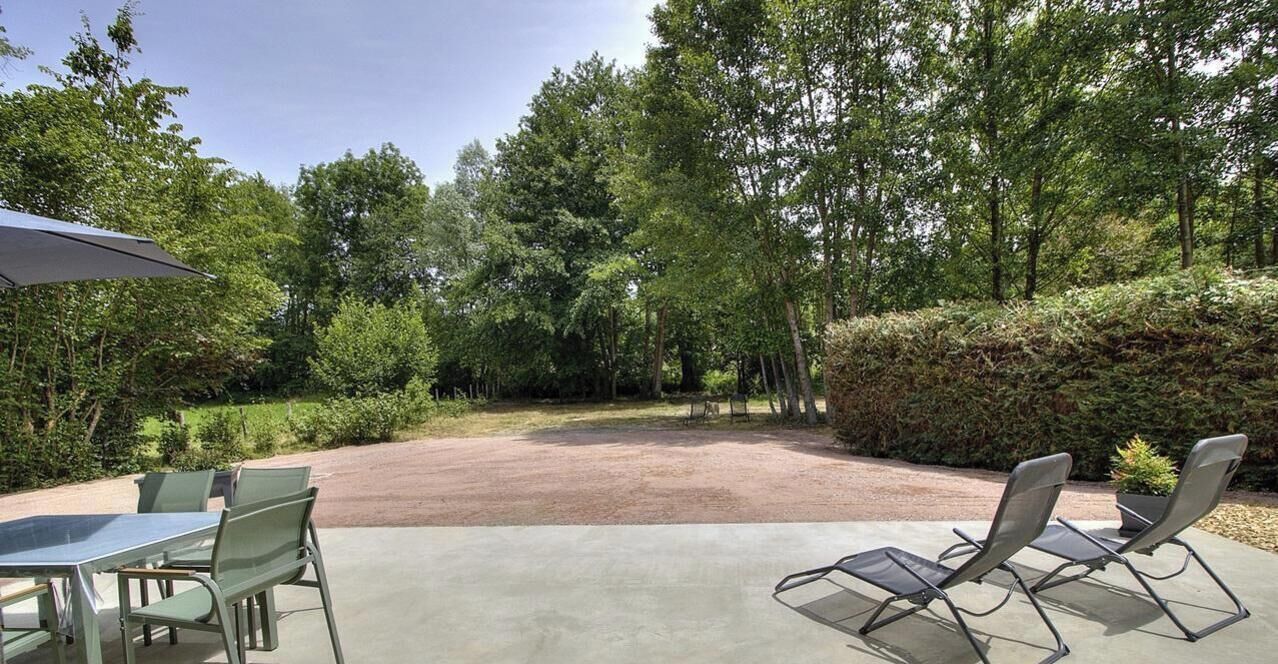 Een terras buiten met een tafel en stoelen, omgeven door groen en bomen.