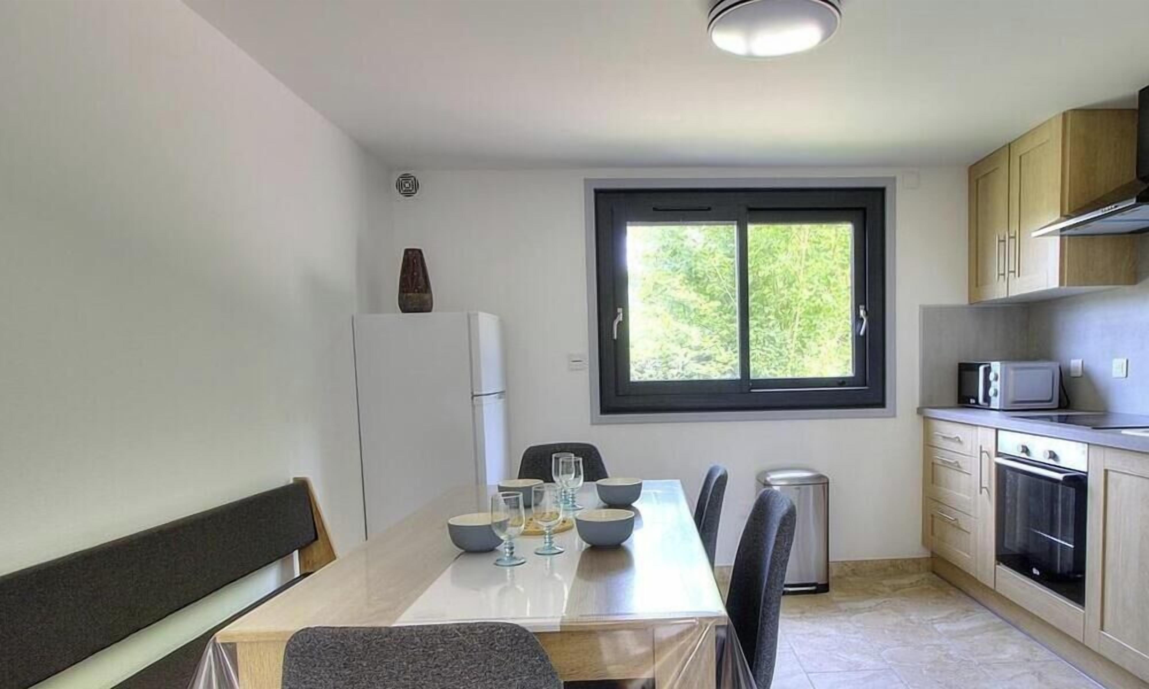 A compact kitchen with a dining area, a window, and a refrigerator.
