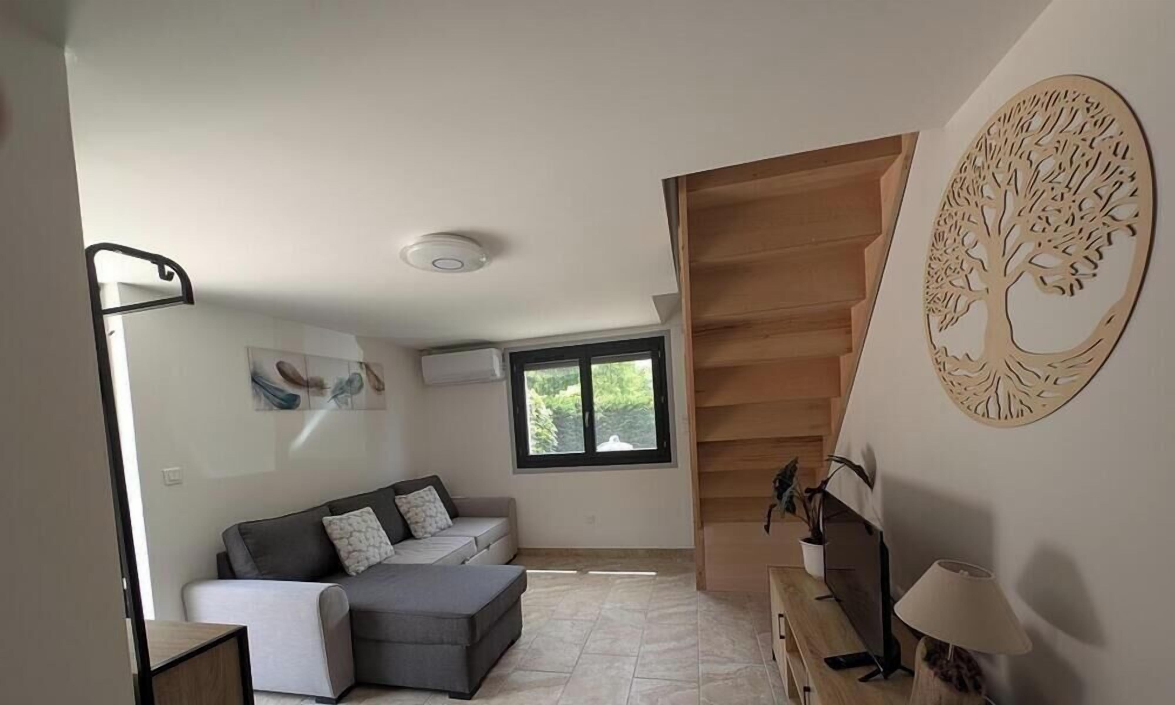 En moderne stue med en grå sofa, et lille bord, en trappe og en trædekoration på væggen.