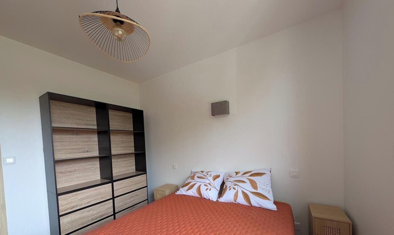 Quarto com cama, prateleira na parede, mesa de cabeceira e luminária pendente.