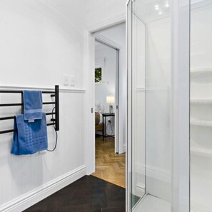 A hallway with a towel rack, a door leading to a room with a bed, and a lamp on a small table. - Wood Street Haven Modern and Walking Distance to Town, Pet Friendly (Greytown)