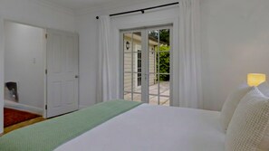 A bedroom with a bed, a green throw, a sliding glass door to a patio, and a lamp on the nightstand. - Wood Street Haven Modern and Walking Distance to Town, Pet Friendly (Greytown)