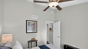 A bedroom with a bed, a ceiling fan, a nightstand, a lamp, and a door leading to another room.