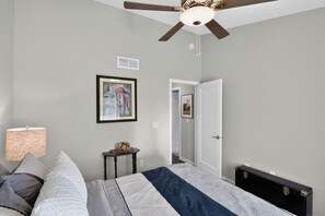 A bedroom with a bed, a ceiling fan, a nightstand, a lamp, and a door leading to another room.