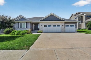 A two-story house with a front driveway, a garage, and a well-maintained lawn. - Spacious 5-Bedroom Home with Hot Tub - Near Kinnick & UIHC (Iowa City)