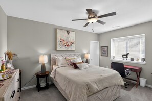A bedroom with a bed, bedside lamps, a desk, a chair, a ceiling fan, and a window with blinds. - Spacious 5-Bedroom Home with Hot Tub - Near Kinnick & UIHC (Iowa City)
