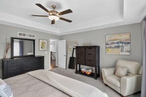 Ein Schlafzimmer mit Bett, Schminktisch, Stuhl, Deckenventilator und Kunstwerken.