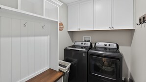 A laundry room with two stacked washers and dryers, white cabinets, and a wooden bench.
