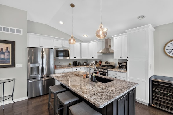 A modern kitchen with stainless steel appliances, a granite countertop, and pendant lighting.