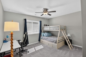 Un dormitorio con literas, escritorio, silla, lámpara y ventilador de techo.
