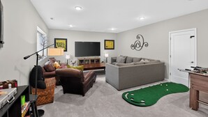 A living room with a sofa, a television, a pool table, and a green carpet.