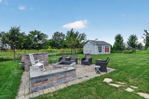 A backyard with a stone fire pit, outdoor furniture, and a small shed. - Spacious 5-Bedroom Home with Hot Tub - Near Kinnick & UIHC (Iowa City)