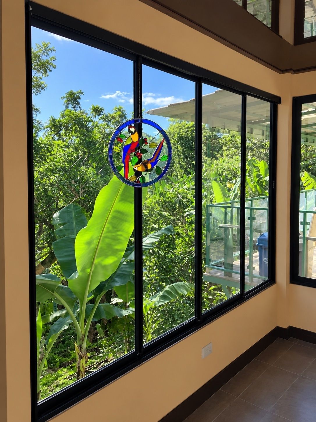 A room with large windows, a view of greenery outside, and a circular stained glass window with a bird design.