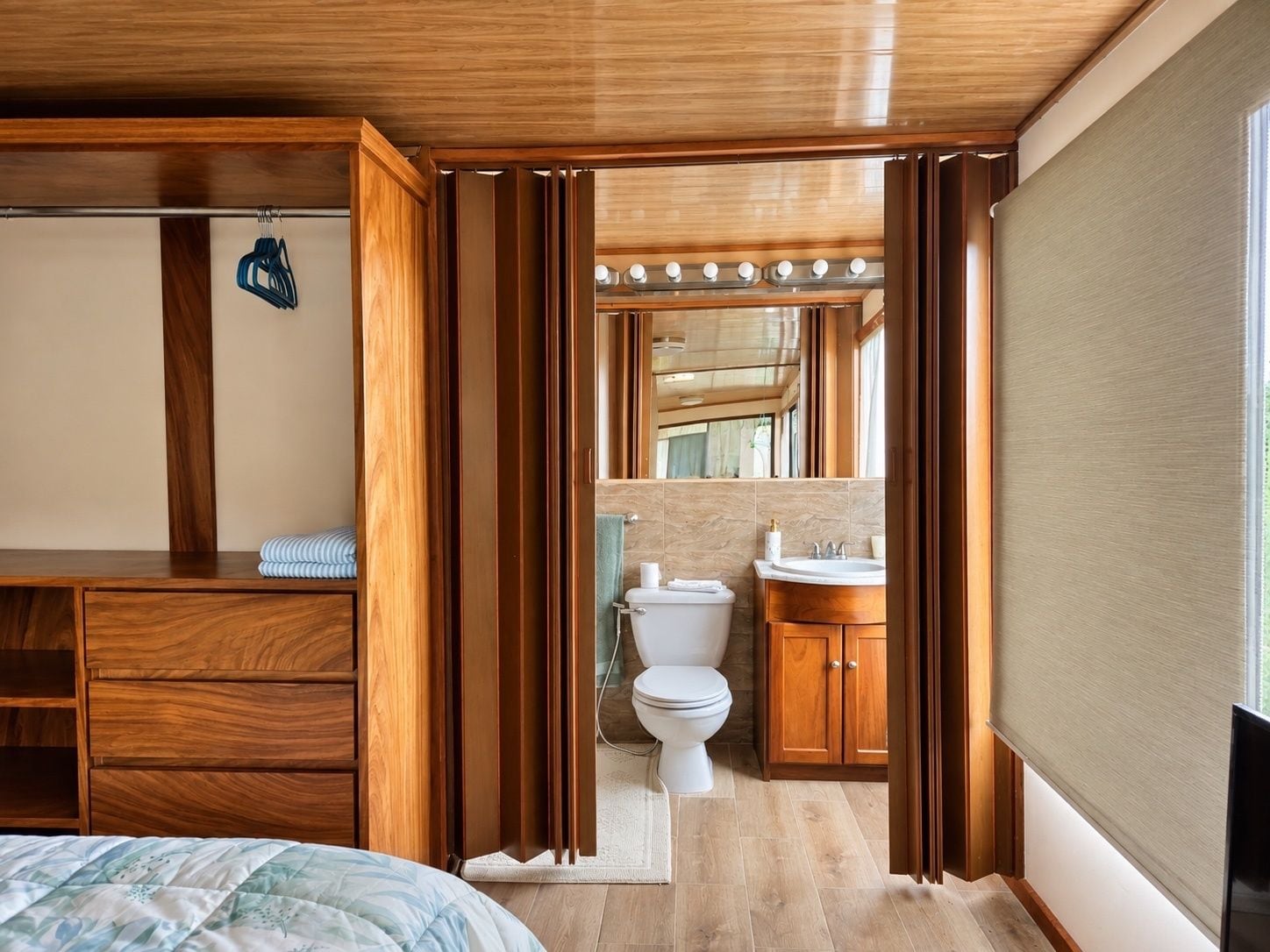 A wooden-framed room with a bed, a bathroom with a toilet, sink, and mirror.