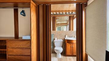 A wooden-framed room with a bed, a bathroom with a toilet, sink, and mirror.