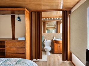 A wooden-framed room with a bed, a bathroom with a toilet, sink, and mirror.
