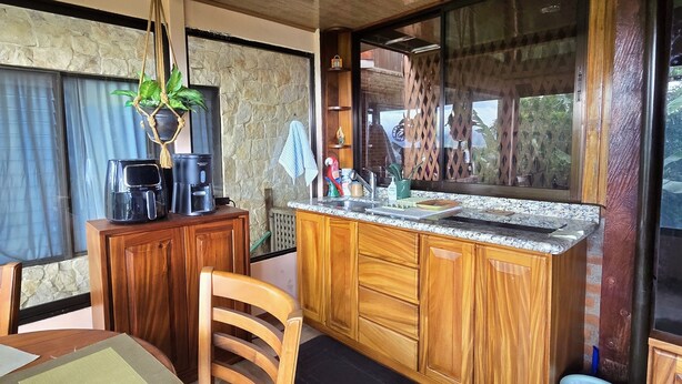 Una cocina con armarios de madera, encimera de granito, planta colgante y comedor con silla y mesa.