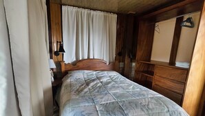Una cama de madera con colcha estampada, cabecera de madera y una mesita de noche con lámpara.