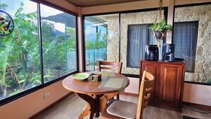 A dining area with a wooden table and chairs, a coffee station, and a view through large windows. - Escazu Studio (San Antonio)