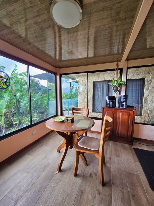 Un espace repas avec une table et des chaises en bois, un coin café et une vue dégagée grâce à de grandes fenêtres.