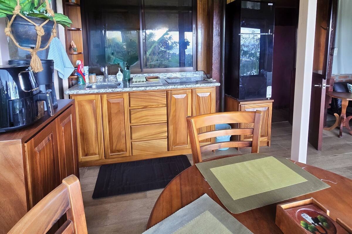 A wooden kitchen with a dining area, wooden cabinets, a coffee maker, and a hanging plant.
