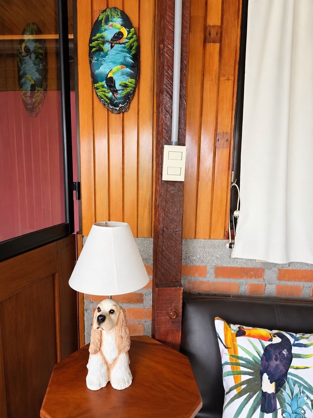 A dog figurine on a wooden table, a lamp, a wall with a painted mural, and a couch with a pillow.