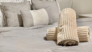 Ein ordentlich bezogenes Bett mit einem beigefarbenen Kopfteil, Kissen und aufgerollten Handtüchern.