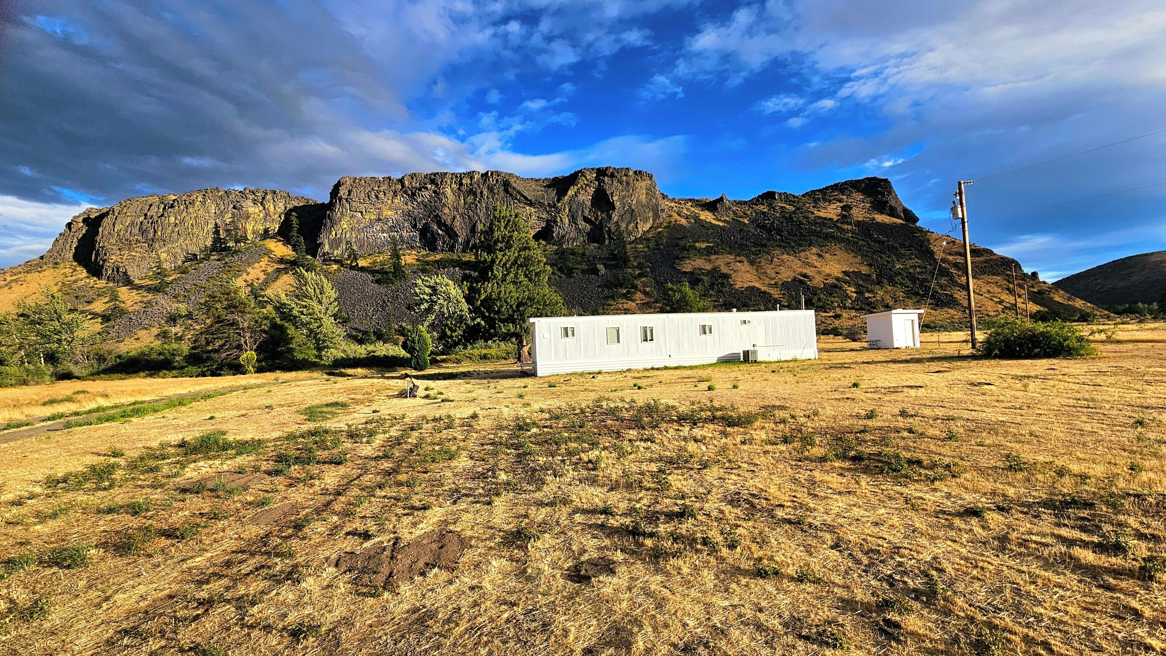 A dry grass field with two white mobile homes and a rocky mountain in the background.