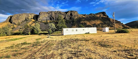 Un campo seco de hierba con dos casas móviles blancas y una montaña rocosa al fondo.
