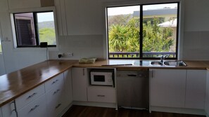 Eine Küche mit Holzarbeitsplatte, einem integrierten Geschirrspüler und einem Fenster mit Blick auf Grünflächen und Gebäude.
