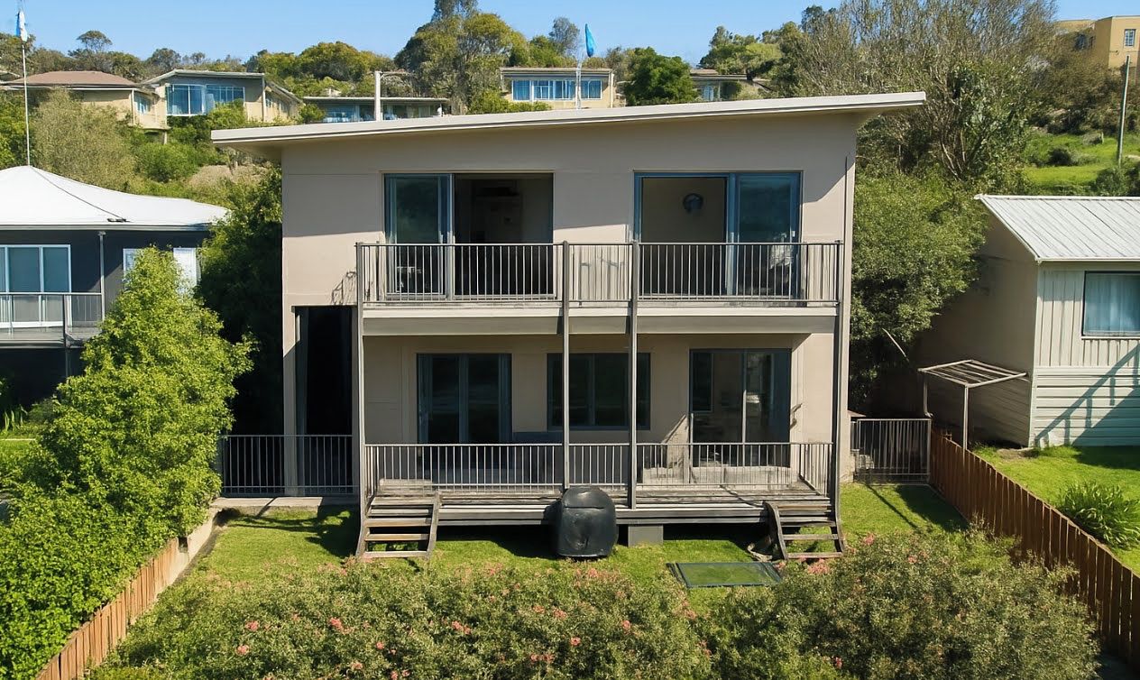 Een gebouw met twee verdiepingen, balkons, een overdekt terras en een omheinde tuin.