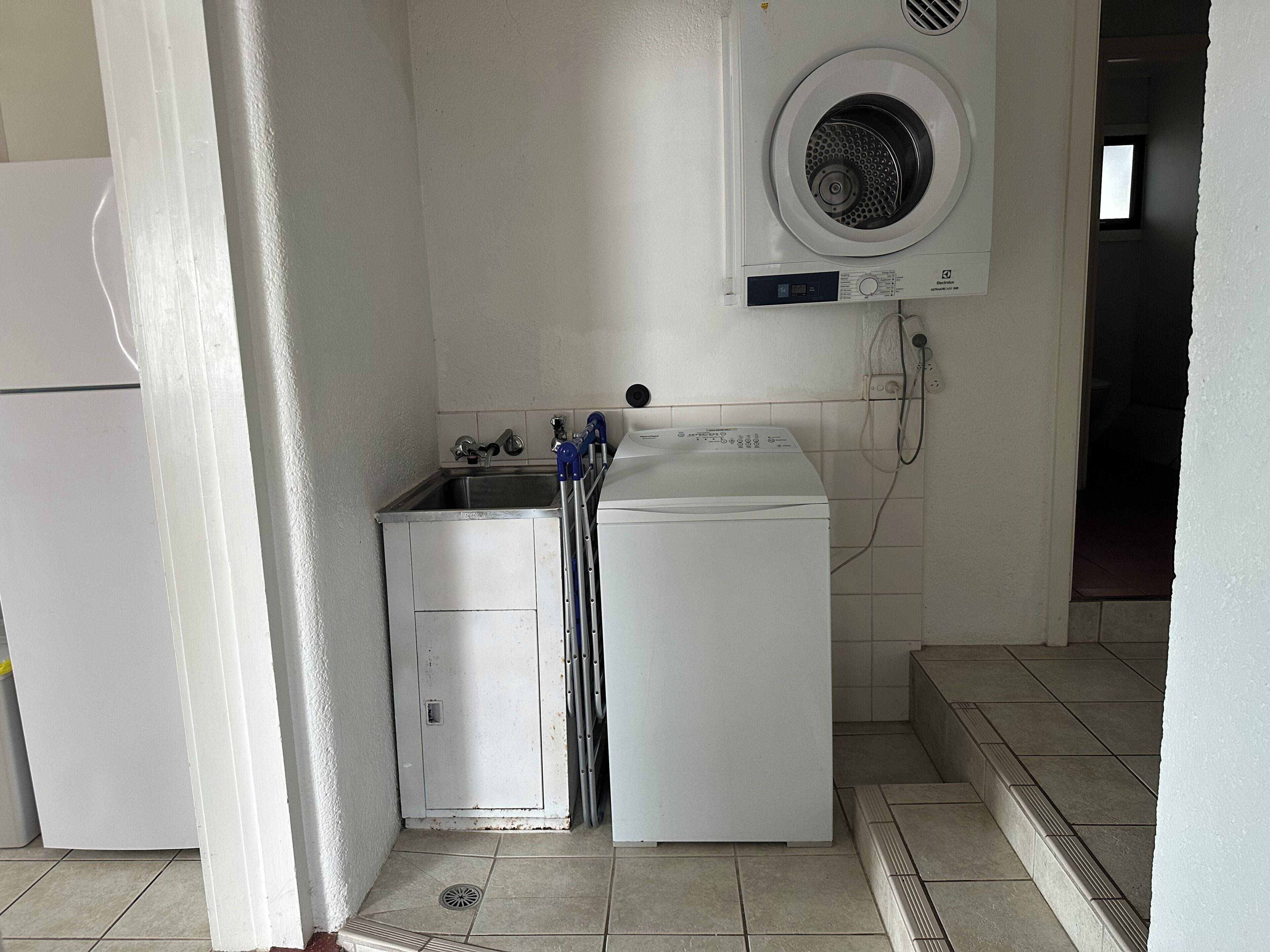 A compact laundry room with a washing machine, a small sink, and a drying machine.