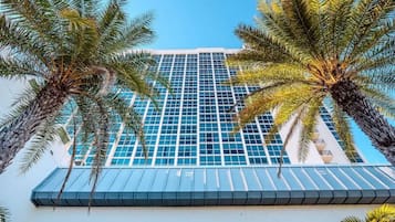 A high-rise building with a glass facade and palm trees in the foreground.