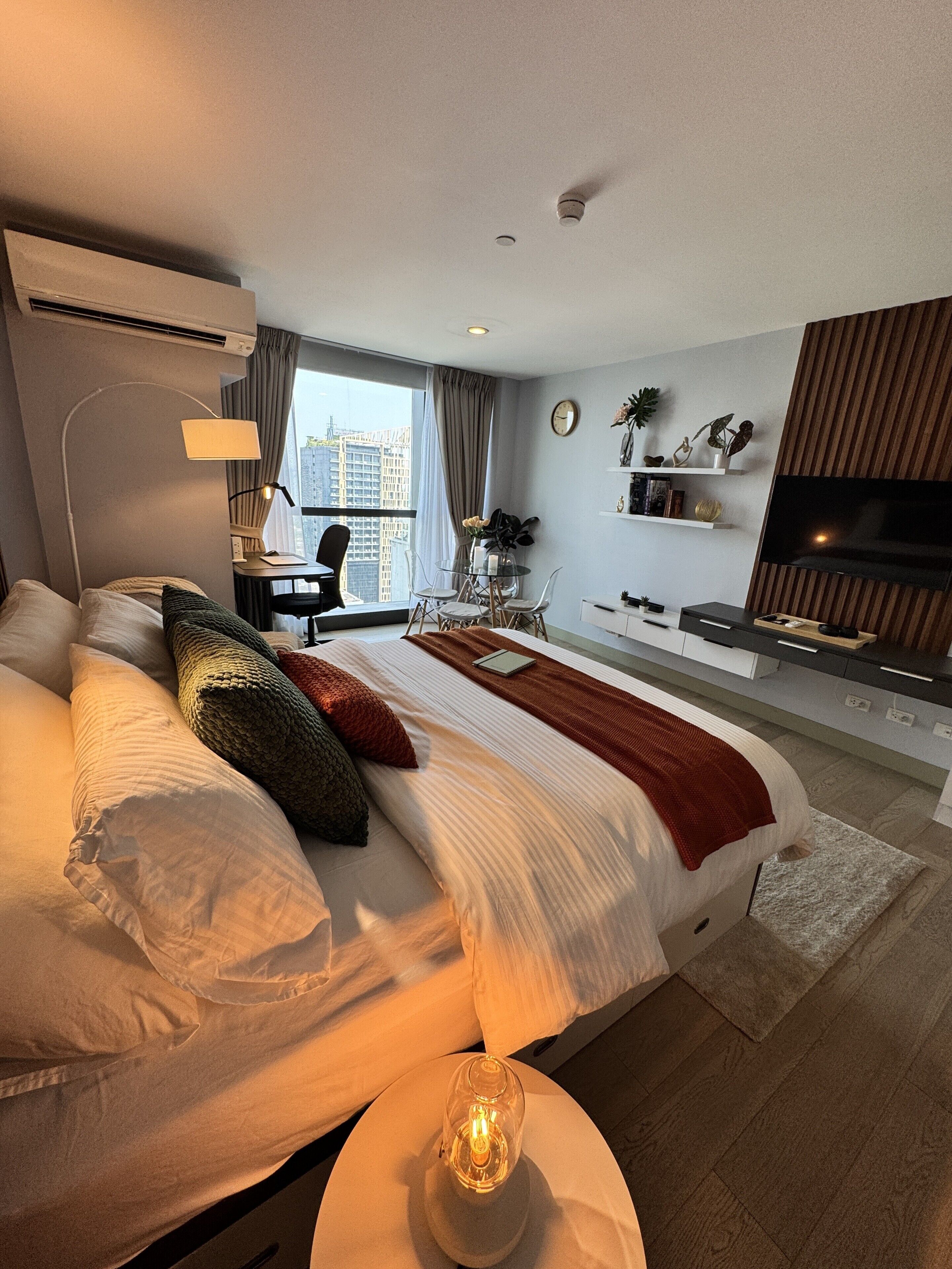 A modern hotel room with a large bed, a desk, a TV, and a city view.