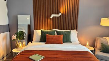 A neatly made bed with a green and orange blanket, a bedside table with a lamp, and a wall-mounted light fixture.
