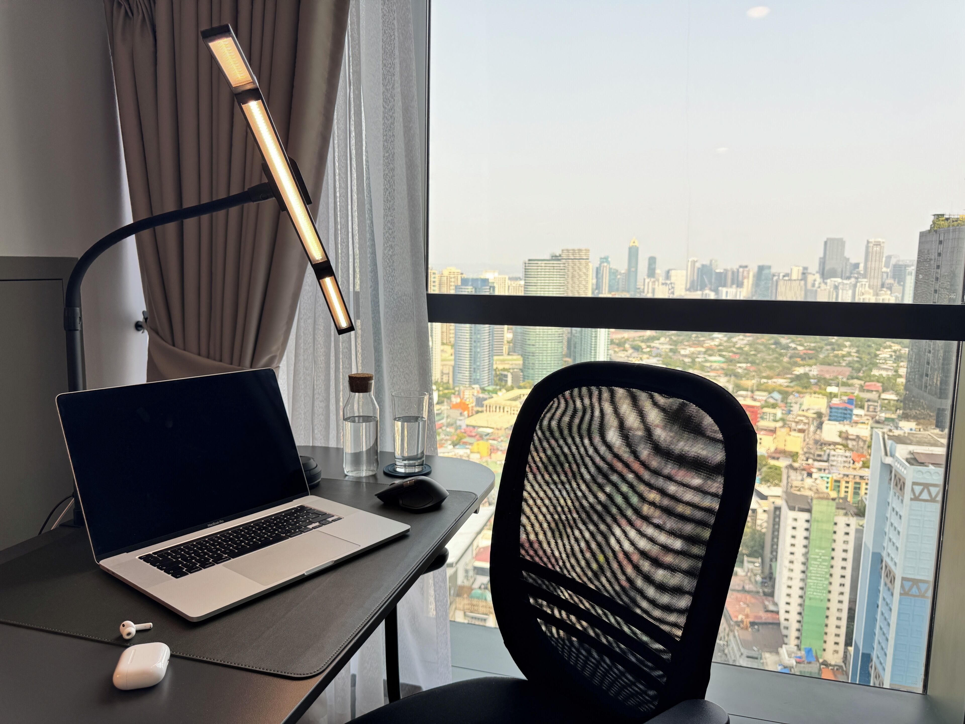 A laptop on a desk with a city view, a lamp, and a chair.