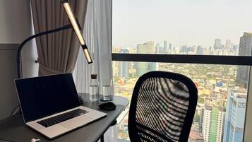 A laptop on a desk with a city view, a lamp, and a chair.
