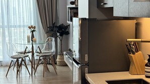 Una cocina moderna con un refrigerador empotrado, un comedor con una mesa y sillas de vidrio, y un ventanal con cortinas.