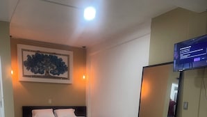 A hotel room with a bed, a television, a mirror, and a tiled floor.