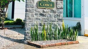 A hotel sign with the name 'Concá' on a stone pillar, surrounded by plants.