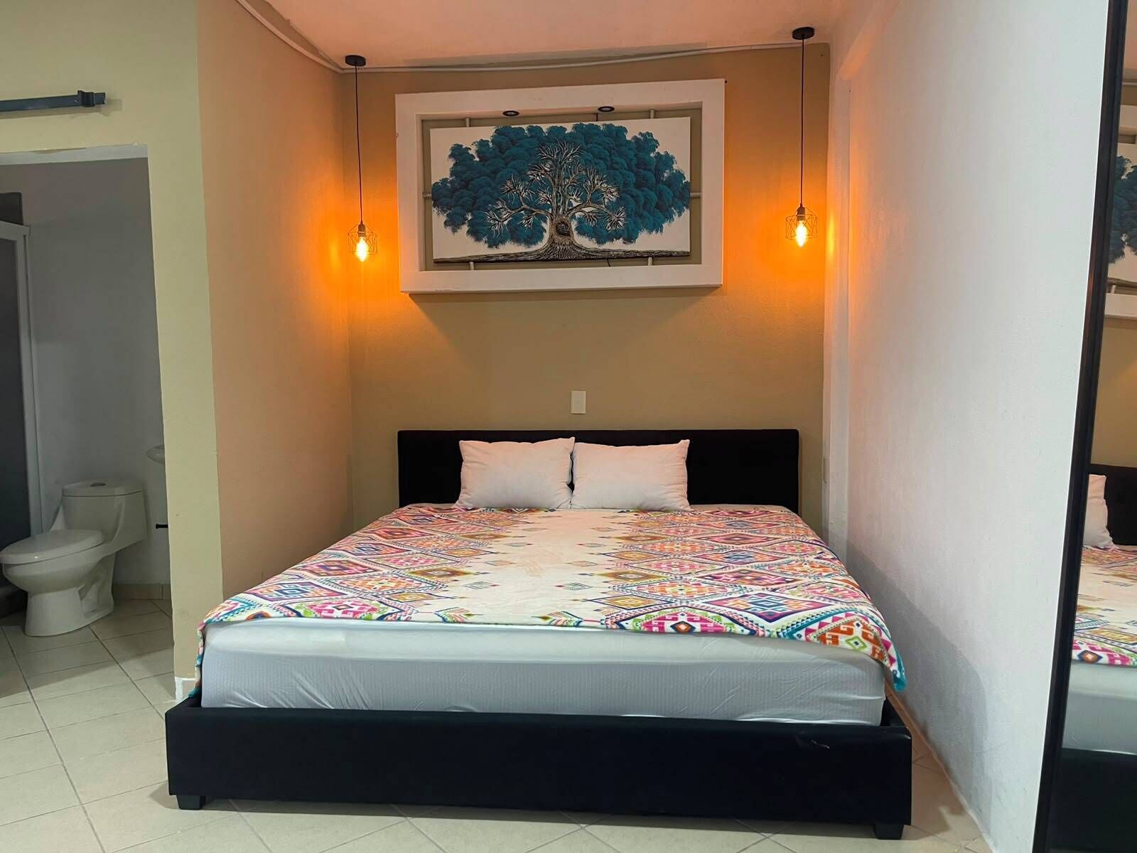 Una cama con un colcha colorida, un cabecero y un cuadro de un árbol colgado en la pared.