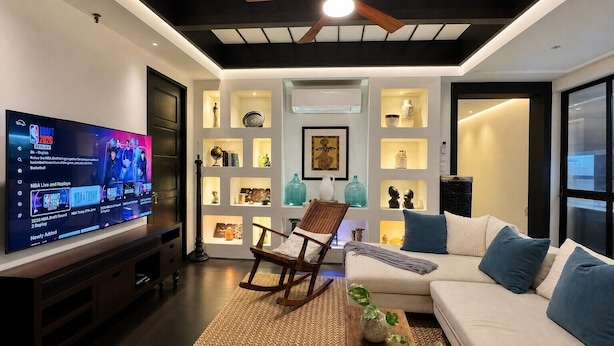 Een moderne woonkamer met een televisie, zitmeubels, decoratieve planken en een plafondventilator.