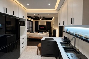 A modern kitchen with a built-in oven, a dining area with a table and chairs, and a living room with a sofa and a TV displaying 'NETFLIX'. - 500Mbps | Sit-Stand Desk | Pro-Kitchen | WD | King (Makati City)