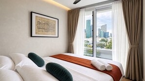 Een hotelkamer met een groot bed, uitzicht over de stad, een ingelijste architectuurtekening en een plafondlamp.