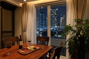 A dining table with a wine bottle, glasses, and a cheese board, set against a cityscape view. - 500Mbps | Sit-Stand Desk | Pro-Kitchen | WD | King (Makati City)