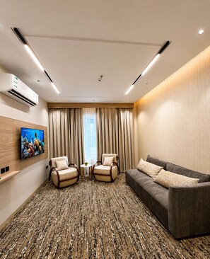Une chambre d’hôtel équipée d’un canapé, de deux fauteuils, d’une télévision et d’un appareil de climatisation.