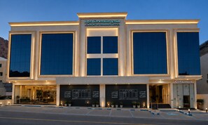 Un hotel con fachada moderna, ventanas amplias y un cartel que indica que se trata del Hotel Al Naqat Al Thamani.