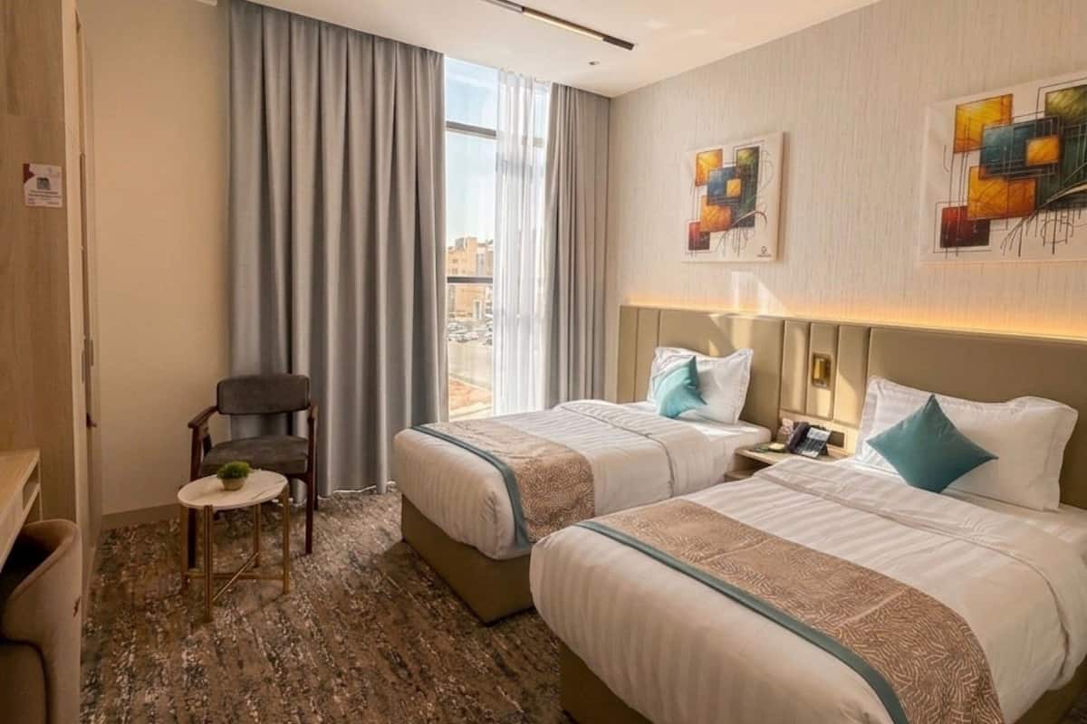 Ein Hotelzimmer mit zwei Betten, einem Sessel, einem kleinen Tisch und Blick auf die Stadt.